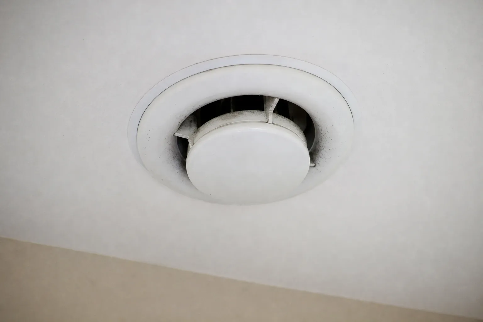 Bouche d'extraction de VMC au plafond d'une pièce, légèrement encrassée