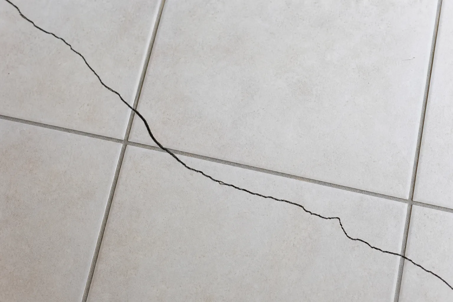 Carrelage interieur clair presentant une fissure traversant plusieurs carreaux apres la pose