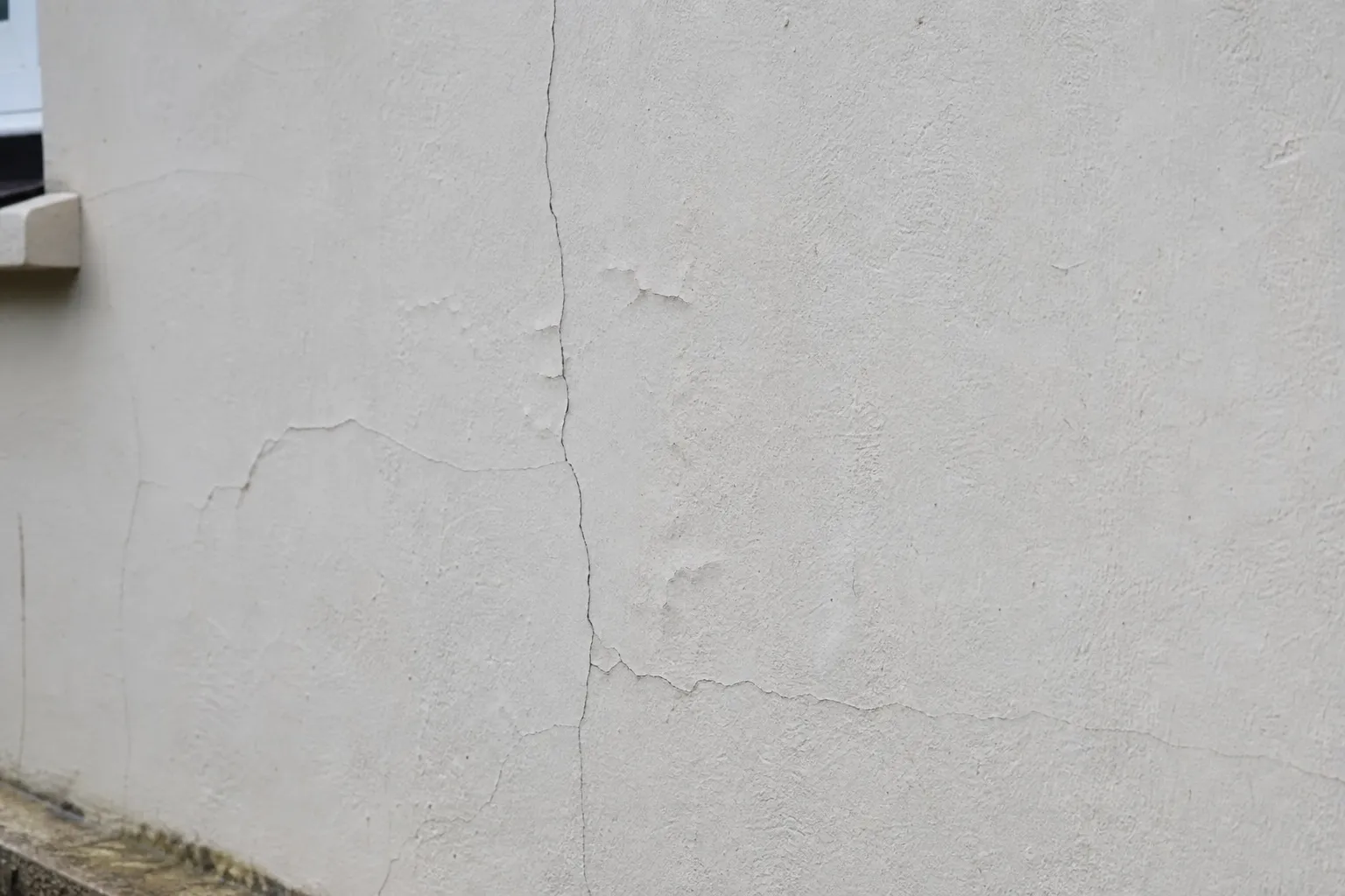 Facade enduite claire presentant des fissures et des cloques a analyser