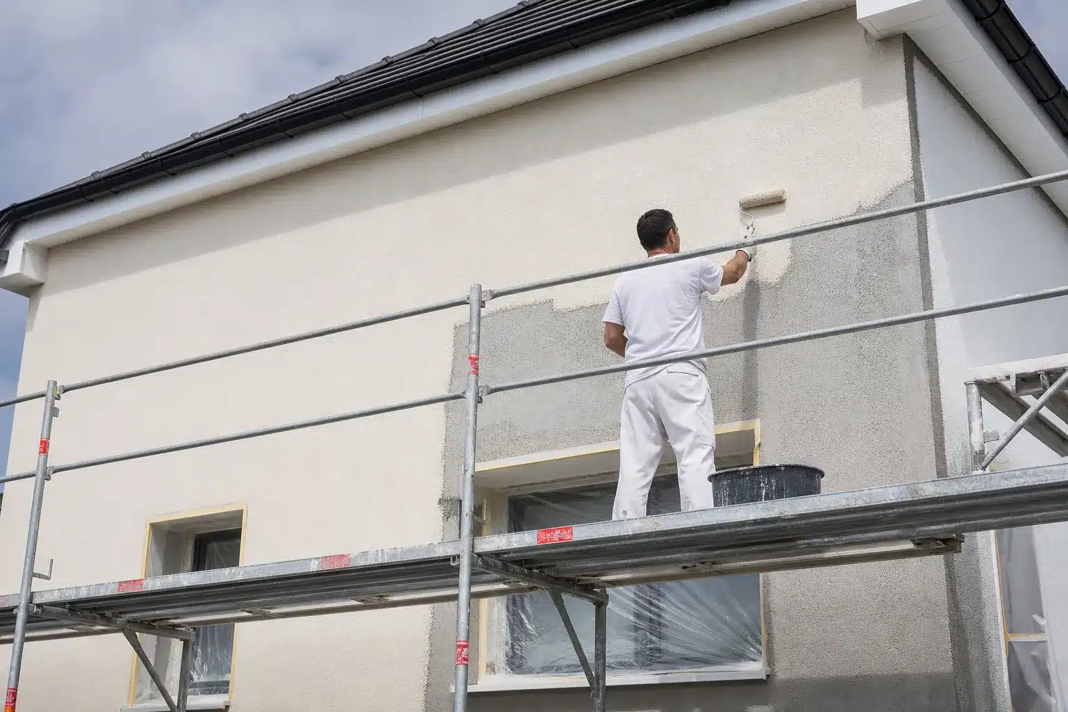 Ravalement de facade d'une maison avec echafaudage et application d'enduit par un ouvrier