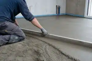 Ouvrier lissant une chape de mortier fraîche à la règle sur le sol d'une pièce en construction