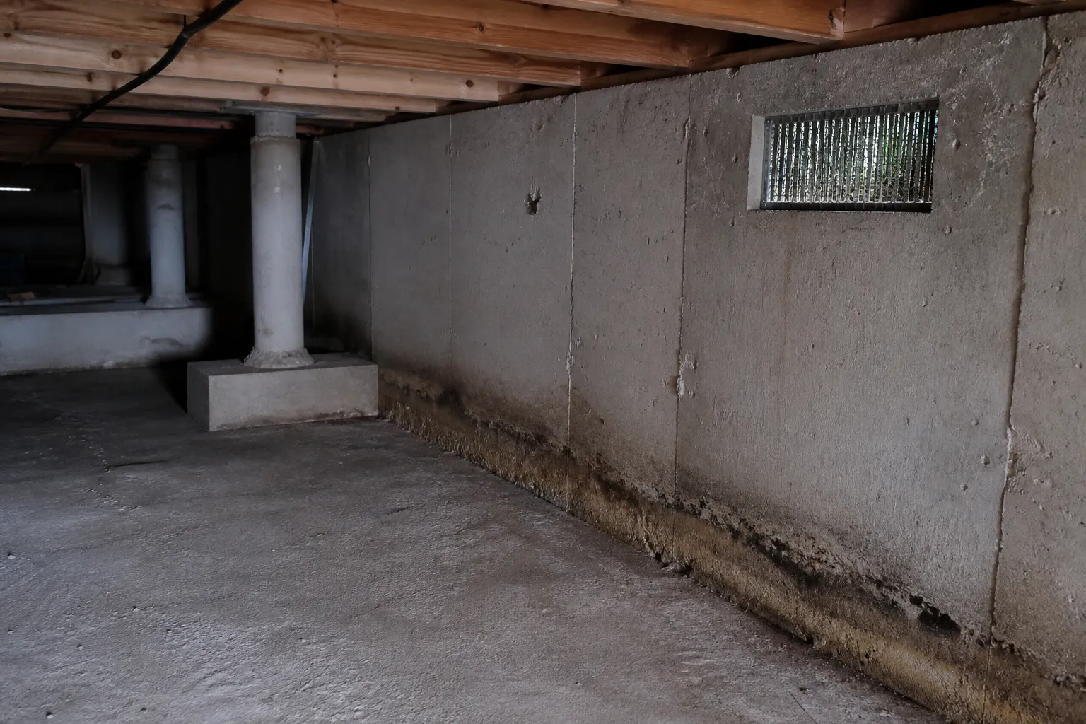 Sous-sol d'une maison avec murs en béton, grille d'aération et fondations visibles