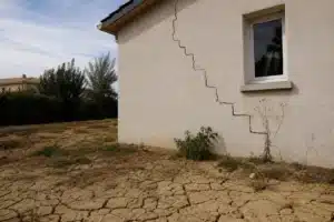 Fissure en escalier sur la façade d'une maison individuelle après la sécheresse, sol argileux craquelé au premier plan