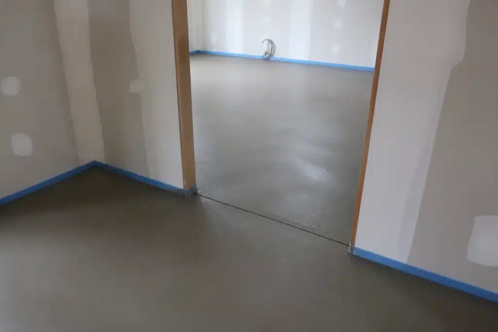 Chape ciment en cours de séchage avec joint de fractionnement au seuil de porte et bande périphérique en pied de mur