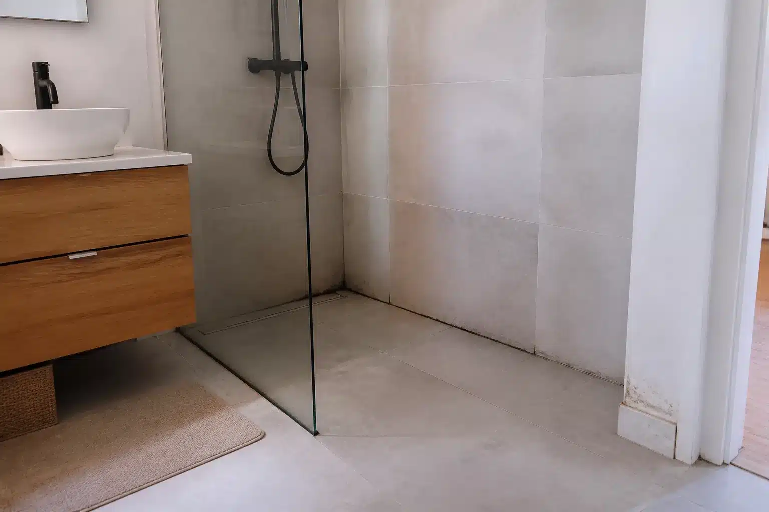 Douche à l'italienne rénovée avec joints noircis dans l'angle et plinthe tachée par l'humidité