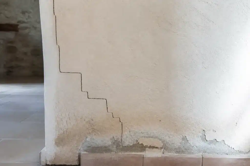Fissure en escalier à la jonction entre une maison ancienne et son extension récente, avec trace d'humidité en pied de mur