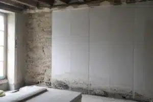 Mur en pierre d'une maison ancienne en partie doublé par l'intérieur, avec auréoles d'humidité et moisissures au pied du doublage