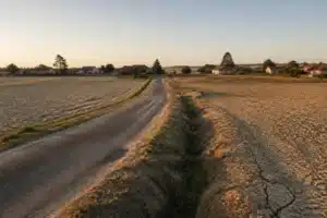 Limite entre deux communes rurales avec maisons individuelles et champs argileux craquelés