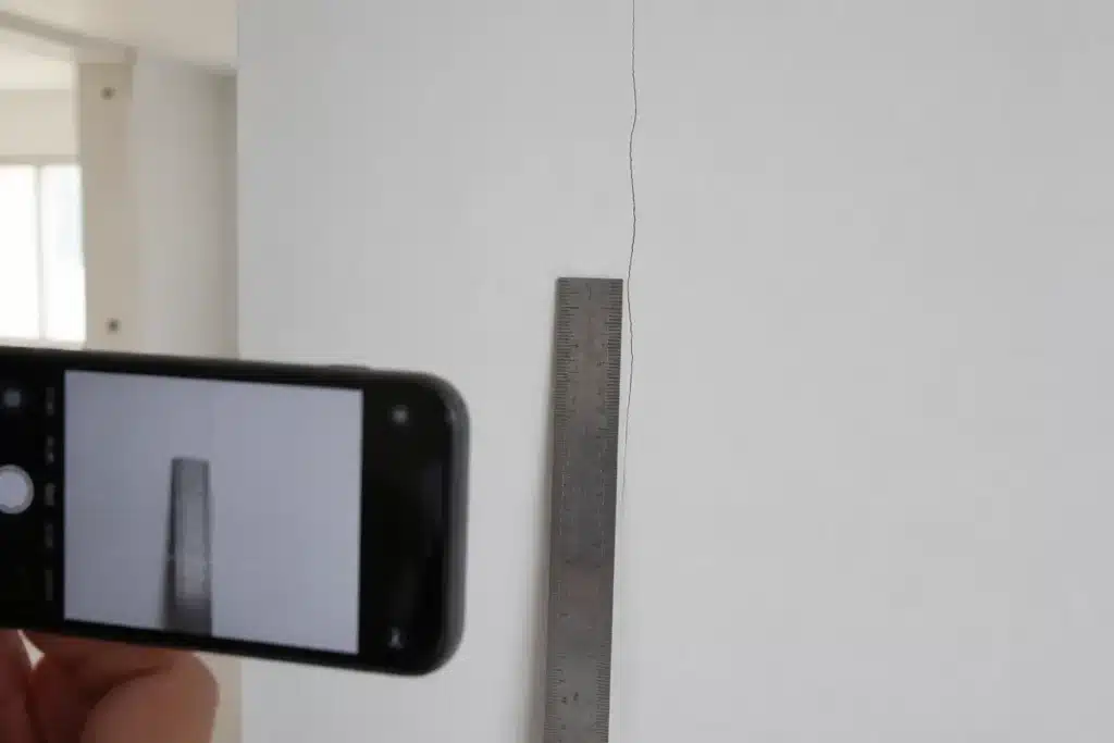 Fissure fine sur une cloison peinte de maison neuve mesurée avec un réglet et photographiée pour un courrier recommandé