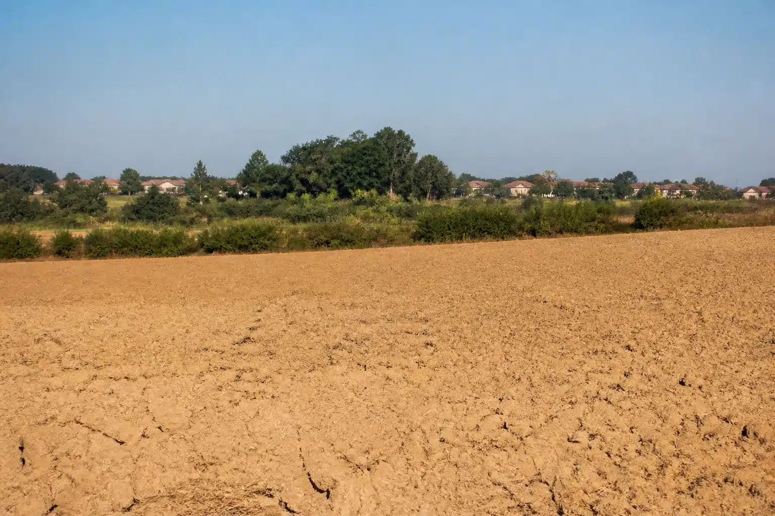 Plaine agricole au sol argileux craquelé avec des maisons individuelles à l'horizon