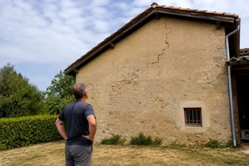 Propriétaire observant une fissure en escalier sur le pignon de sa maison