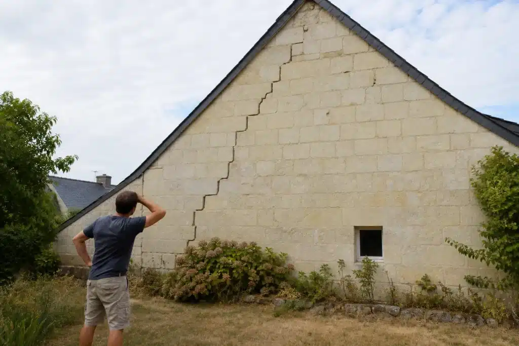 Propriétaire observant une fissure en escalier sur le pignon de sa maison