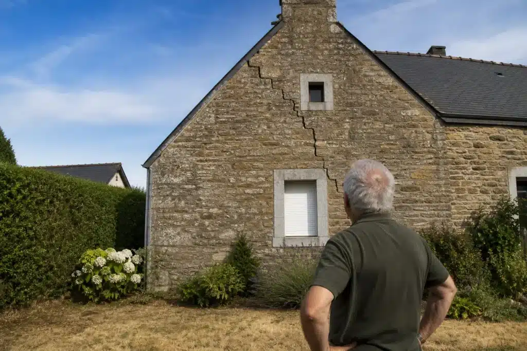Propriétaire observant une fissure en escalier sur le pignon de sa maison