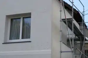 Façade de maison fraîchement ravalée avec échafaudage, enduit clair présentant des fissures réapparues et une zone de peinture cloquée