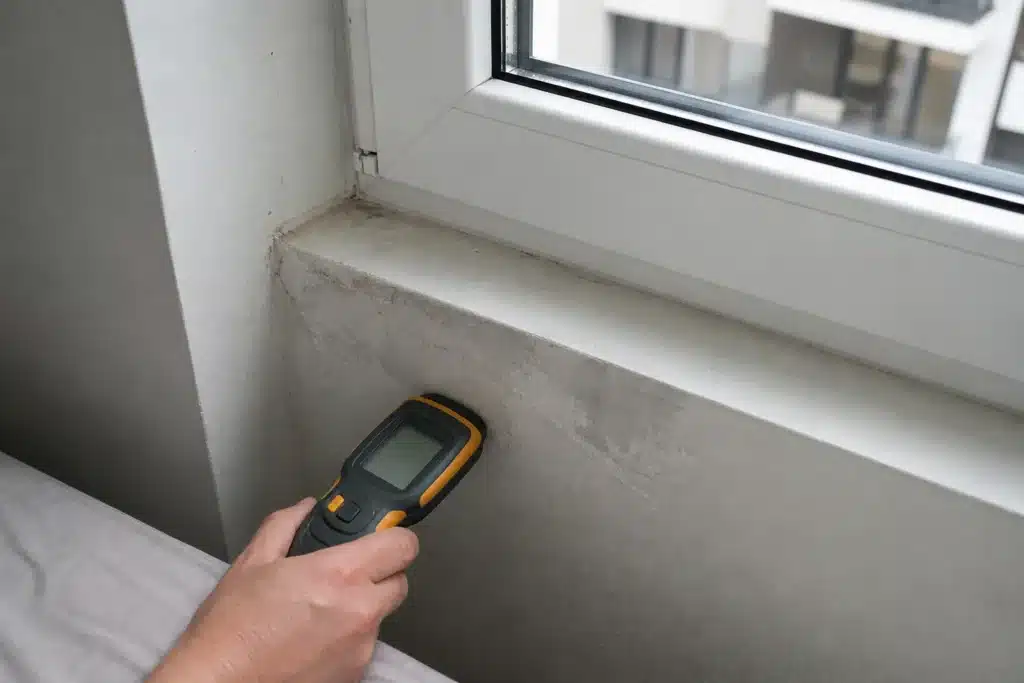 Trace d'humidité et peinture cloquée sous une fenêtre d'appartement neuf, mesure à l'humidimètre