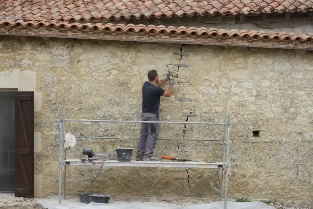 Maçon réalisant une reprise de fissure par agrafage sur un mur