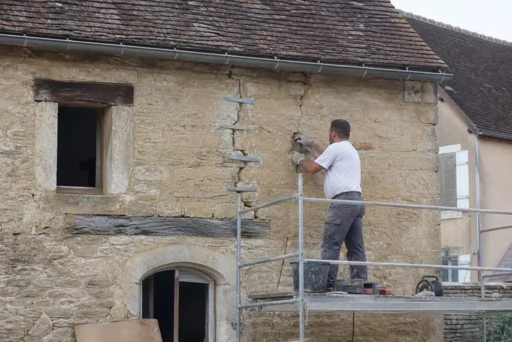 Maçon réalisant une reprise de fissure par agrafage sur un mur