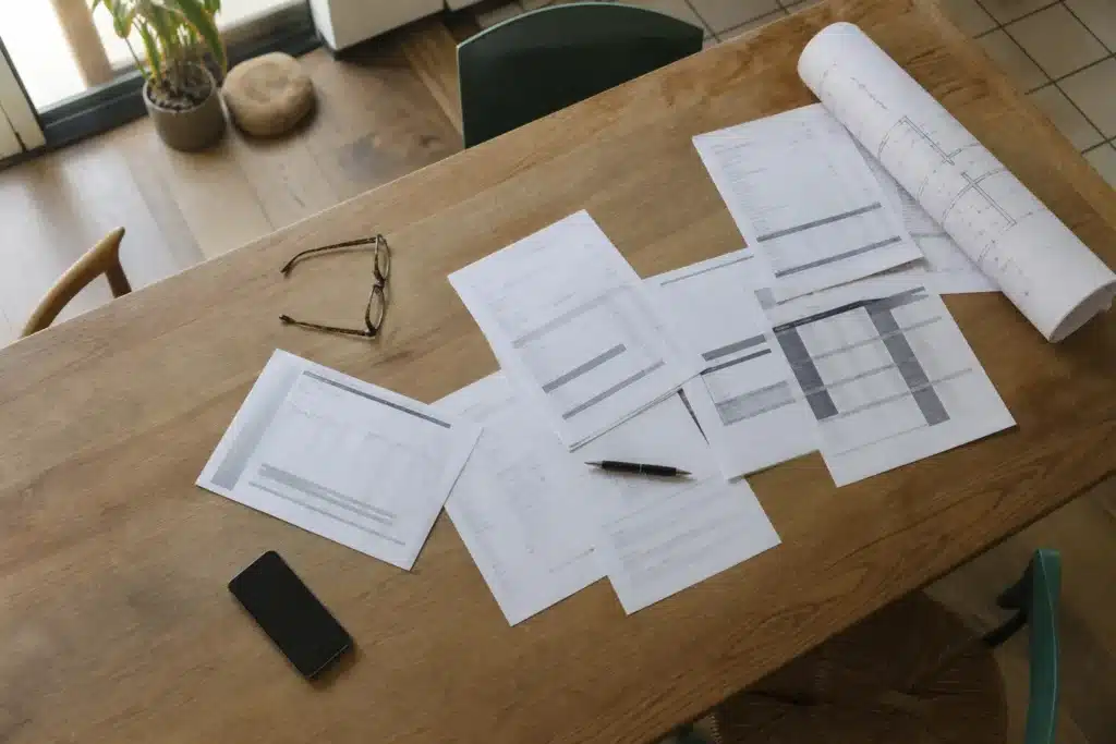 Devis de travaux, facture et attestation d'assurance posés sur une table de cuisine à côté de plans de rénovation, prêts à être vérifiés